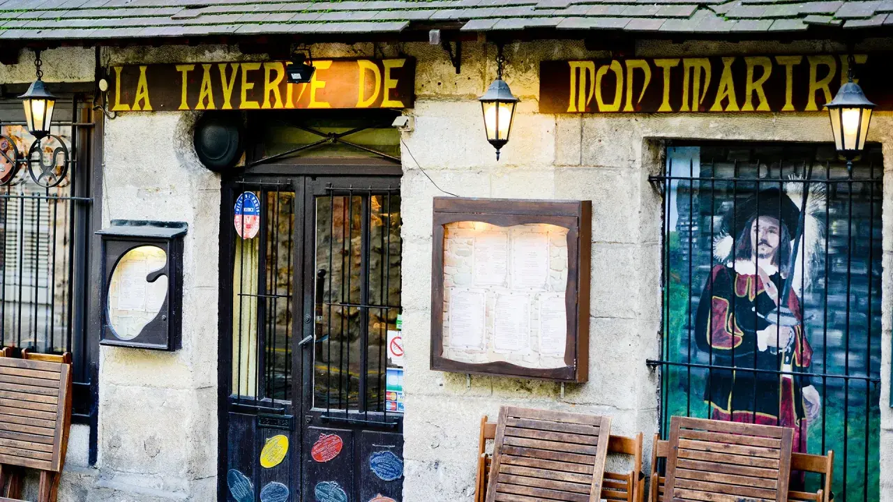 La taverne de Montmartre, une définition de l'ambiance parisienne. Façade de pierre, enseigne jaune, menu affiché, et une peinture murale d'un mousquetaire.