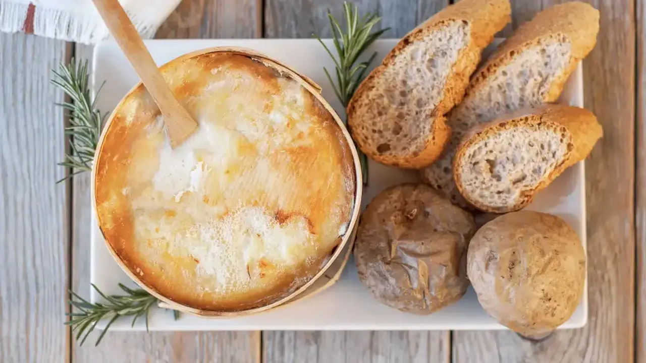 Un fromage à raclette fondant, une spécialité Jura, servi avec du pain croustillant et des pommes de terre.