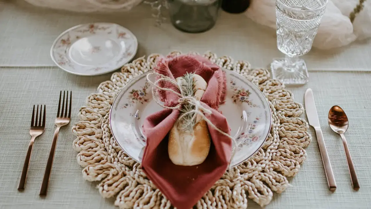 Une table dressée avec élégance, une assiette fleurie, une serviette bordeaux et une **fourchette à la française** en cuivre, prête pour un repas raffiné.