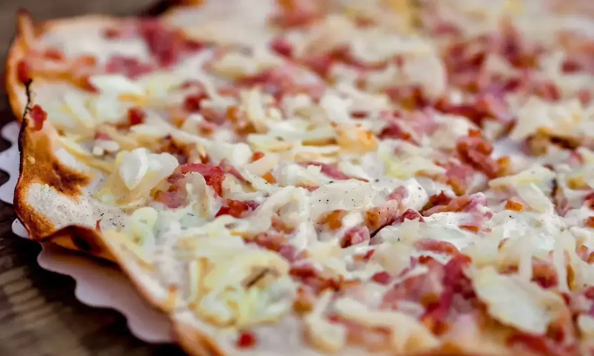 Tarte flambée gourmande, spécialité d'un restaurant alsacien à Nantes. Crème, lardons et oignons sur une pâte fine et croustillante.