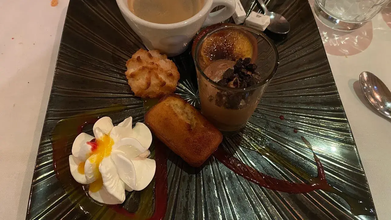 Un assortiment gourmand : café, financier, macaron, verrine chocolat et chantilly, servi sur une assiette noire texturée, digne de la taverne des fougères.