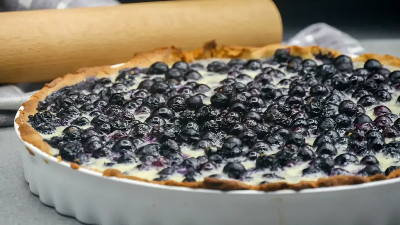 Tarte aux myrtilles traditionnelle, garnie de fruits frais et d'une crème onctueuse, prête à être dégustée.