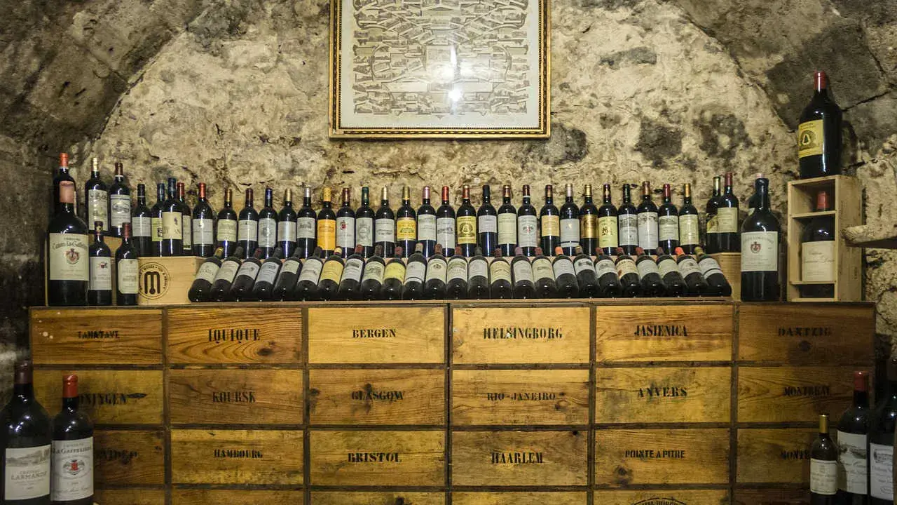 Cave voûtée avec une carte ancienne au mur, présentant une impressionnante liste des grands vins de Bourgogne, rangés sur des caisses en bois.