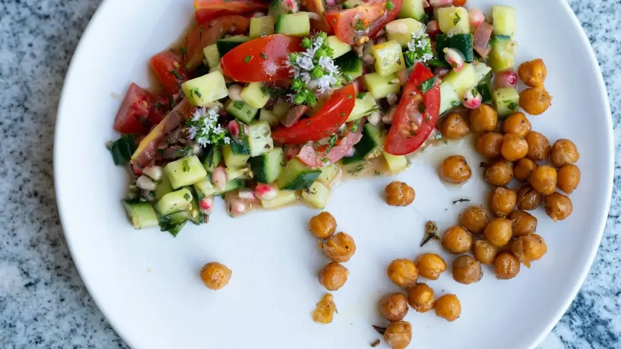 Salade colorée de tomates, concombres et pois chiches rôtis, garnie de petites fleurs blanches.