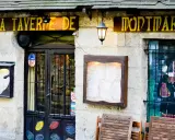 La taverne de Montmartre, une définition de l'ambiance parisienne. Façade de pierre, enseigne jaune, menu affiché, et une peinture murale d'un mousquetaire.