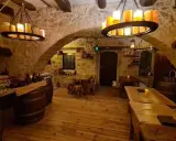 Intérieur d'une taverne médiévale avec murs en pierre, tables en bois et chandeliers. Le tavernier moyen âge y servirait sûrement de l'hydromel.