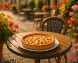 Une quiche lorraine dorée, spécialité de Metz, sur une table de terrasse fleurie.