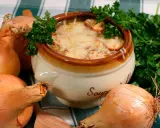 Un bol de soupe à l'oignon gratinée, un plat parisien réconfortant, entouré d'oignons frais et de persil.
