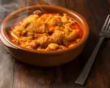 Un plat fumant de tête de veau mijotée dans une sauce rouge, rappelant la recette tête de veau grand-mère. Une fourchette est posée à côté.