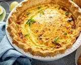 Une délicieuse quiche lorraine, un classique des plats lorrains, garnie de feuilles vertes.