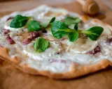 Tarte flambée alsacienne garnie de lardons, fromage de chèvre et jeunes pousses.