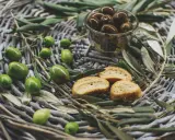 Olives vertes et noires, crostinis et feuilles d'olivier sur un panier tressé, évoquant une spécialité culinaire du Luberon.
