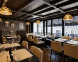 Salle à manger élégante avec des tables dressées, des luminaires Tiffany et une affiche "Les Artistes Limoges Menu" au mur.