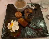 Un assortiment gourmand : café, financier, macaron, verrine chocolat et chantilly, servi sur une assiette noire texturée, digne de la taverne des fougères.