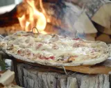 Flammekueche dorée et fumante, garnie de lardons et de fromage fondant, cuite au feu de bois.