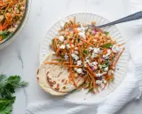 Salade de pois chiches et carottes râpées assaisonnement frais, garnie de feta émiettée et servie avec du pain plat.