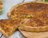 Une part de quiche lorraine, plat originaire de Lorraine, dorée et appétissante, sur une planche en bois. Des œufs frais sont visibles en arrière-plan.