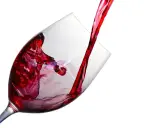 Un jet de vin rouge tourbillonne dans un verre à beaujolais, créant des éclaboussures vibrantes.
