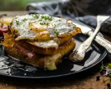 Un croque-madame gourmand, un des plats typiques parisiens, avec un œuf au plat, jambon et fromage fondant, servi avec des tomates et des pousses.