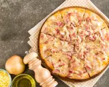 Flammekueche gourmande, garnie de lardons et d'oignons sur une base de fromage blanc crémeux. Un délice croustillant.