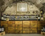 Cave voûtée avec une carte ancienne au mur, présentant une impressionnante liste des grands vins de Bourgogne, rangés sur des caisses en bois.