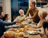Une famille partage un repas joyeux. La mère sert la salade, et tout le monde sourit. C'est un moment de partage, alors pourquoi ne pas mettre les coudes sur la table ?