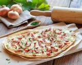 Flammekueche prête à être dégustée, avec ses oignons, lardons et ciboulette. Une recette facile pour un repas convivial.