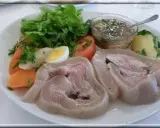 Une assiette de tête de veau gastronomique, accompagnée de légumes frais, d'un œuf dur, de carottes et d'une sauce savoureuse.