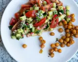 Salade colorée de tomates, concombres et pois chiches rôtis, garnie de petites fleurs blanches.