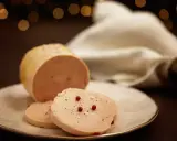 Tranche de foie gras, une des spécialités culinaires Dordogne, assaisonnée de poivre et de baies roses sur une assiette blanche.