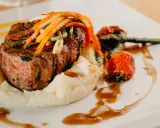 Un plat de viande grillée, purée de pommes de terre et légumes, une des spécialités d'Aurillac, servi sur une assiette blanche avec une sauce brune.