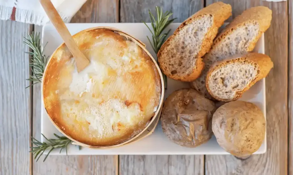 Un fromage à raclette fondant, une spécialité Jura, servi avec du pain croustillant et des pommes de terre.