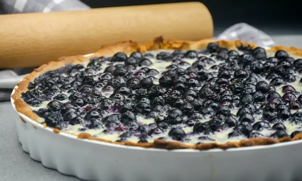 Tarte aux myrtilles traditionnelle, garnie de fruits frais et d'une crème onctueuse, prête à être dégustée.