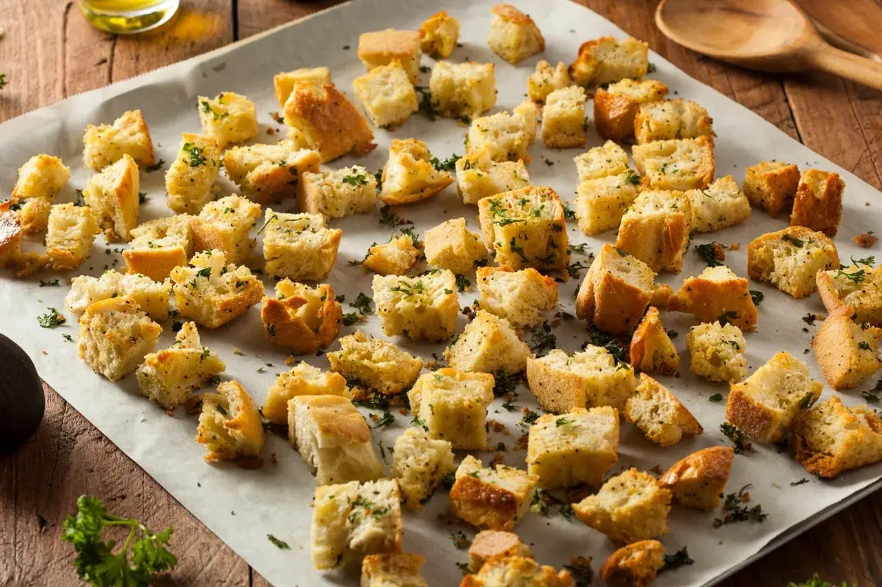 Des morceaux de pain grillés, parsemés d'herbes, prêts à garnir une salade. Ces croutons maison sont un délice croustillant.