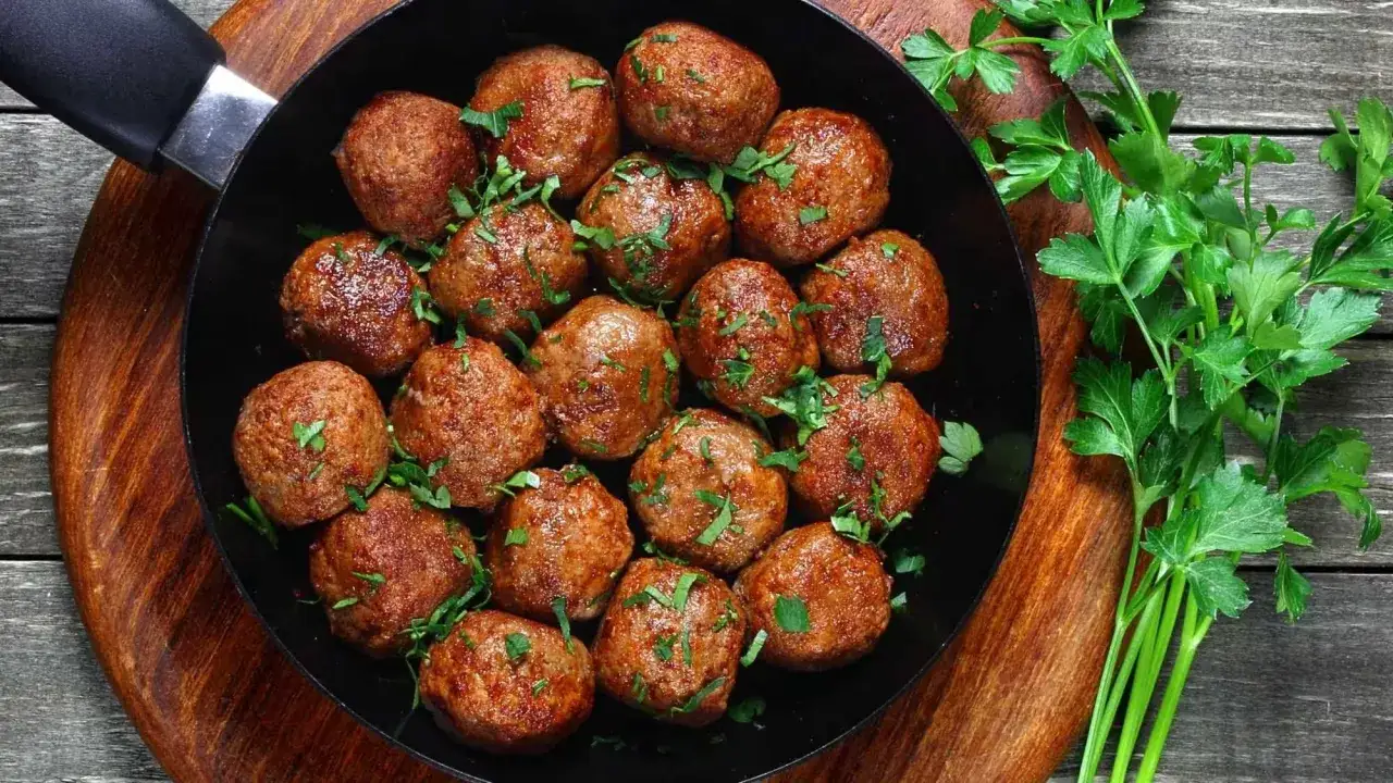 Poêle remplie de fricadelles de bœuf dorées, garnies de persil frais, sur fond de bois.