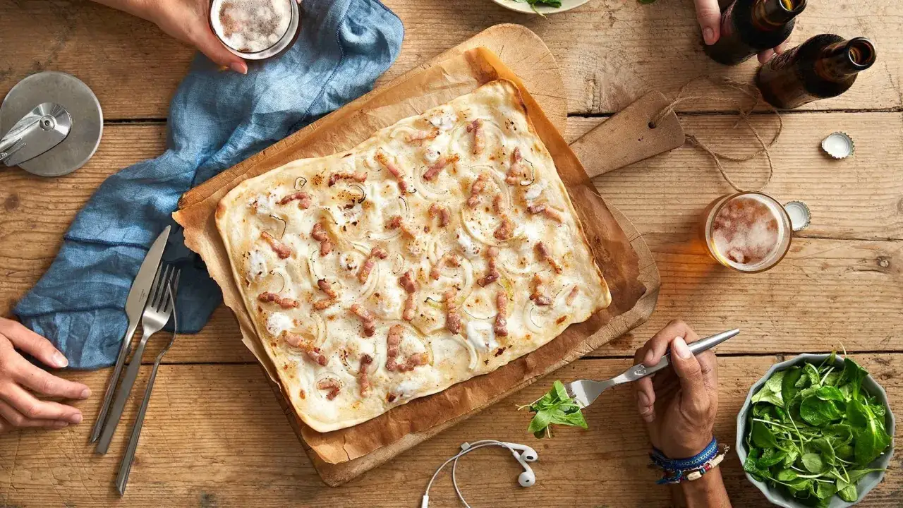 Tarte flambée garnie d'oignons et lardons, prête à être dégustée avec une bière fraîche. Une ambiance de restaurant alsacien à Nantes.