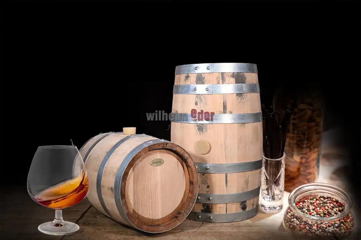 Verre de cognac ambré près de tonneaux en bois, évoquant le meilleur cognac. Amandes et grains de poivre en arrière-plan.