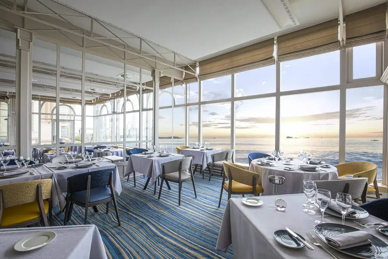 Tables dressées dans un restaurant de Saint-Malo, avec vue panoramique sur la mer au coucher du soleil.