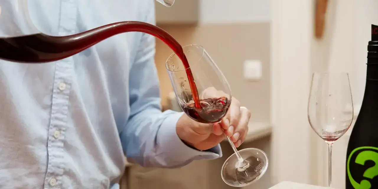 Un homme verse du vin rouge d'une carafe dans un verre. L'action de décanter le vin permet d'aérer et de séparer les éventuels dépôts.
