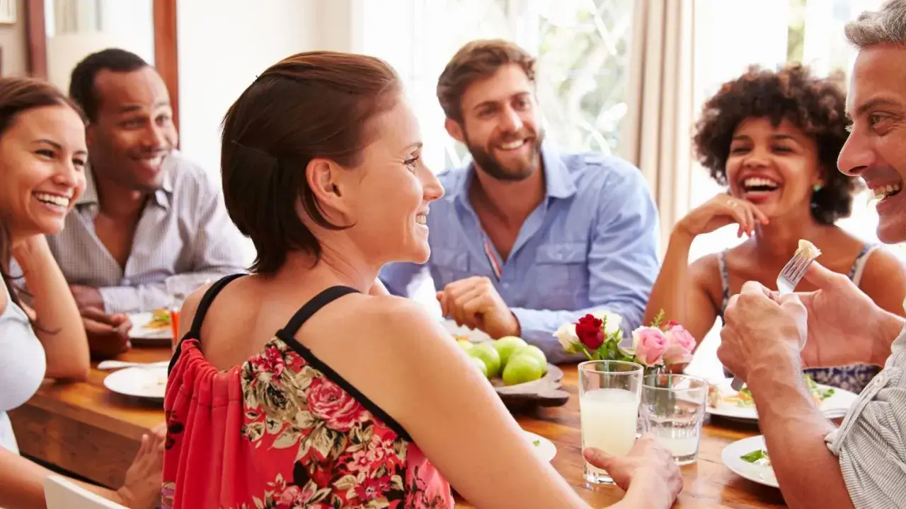 Un groupe d'amis partage un repas joyeux, une excellente idée repas entre collègues travail. Ils rient et discutent autour d'une table en bois.