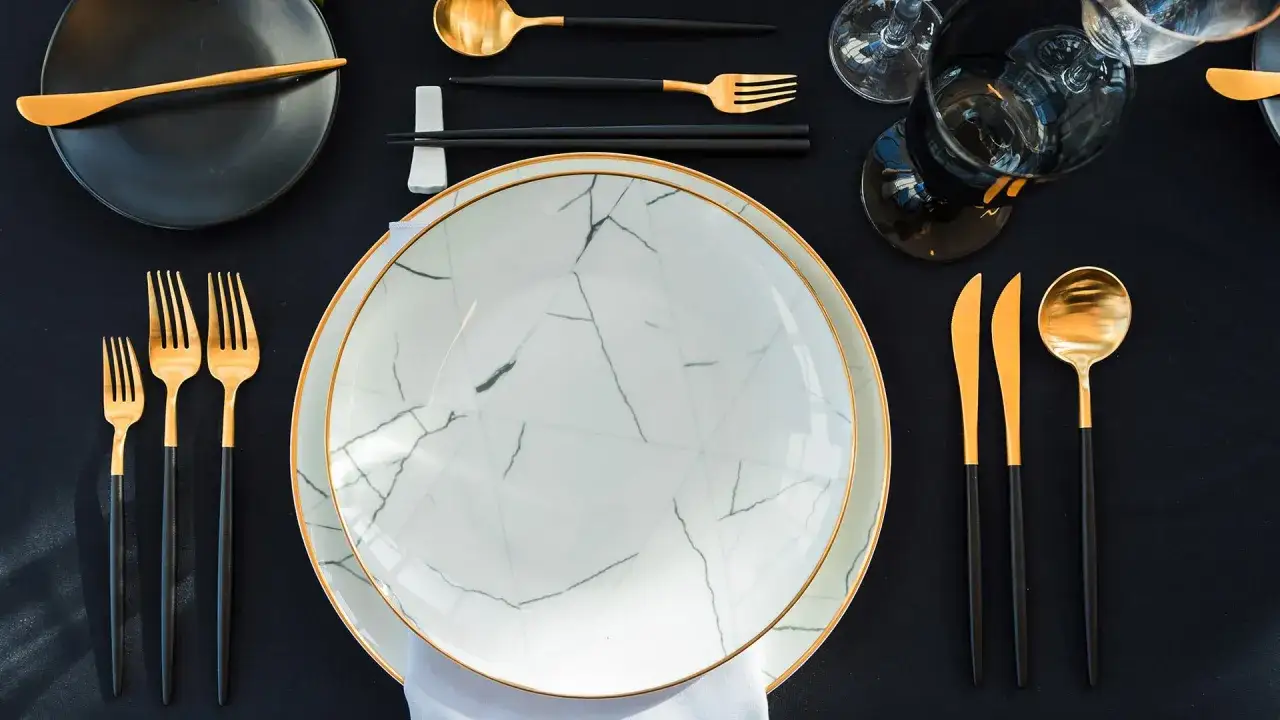 Un magnifique art de la table à la française : assiettes marbrées, couverts dorés et noirs, verres élégants sur une nappe sombre.