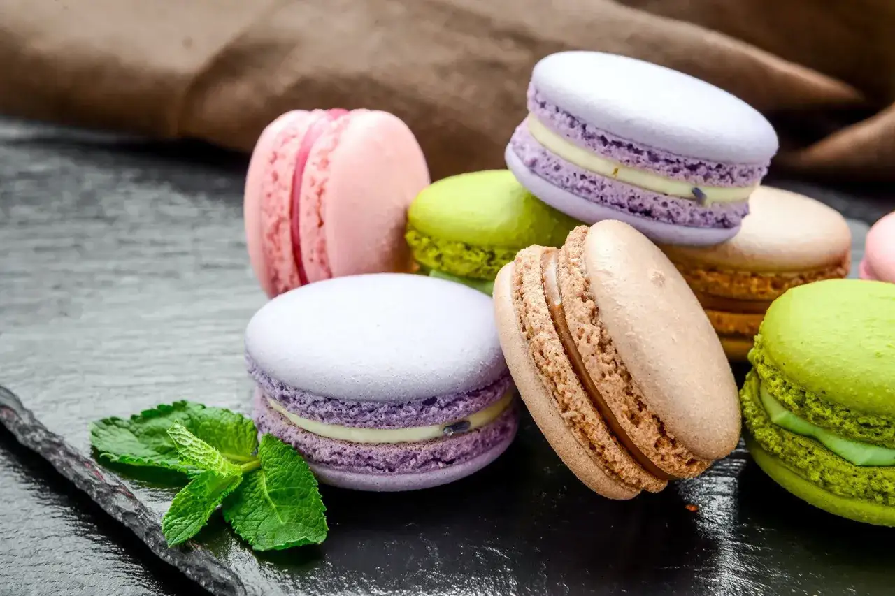 Délicieux macarons aux couleurs vives, une spécialité culinaire parisienne, accompagnés d'une gousse de vanille et de menthe fraîche.