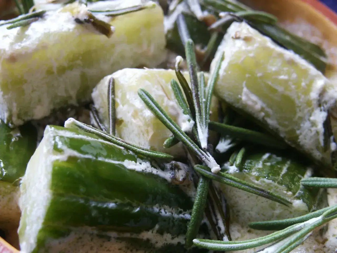 Morceaux de concombre cuit enrobés d'une sauce crémeuse, parsemés de brins de romarin frais. Un plat réconfortant.