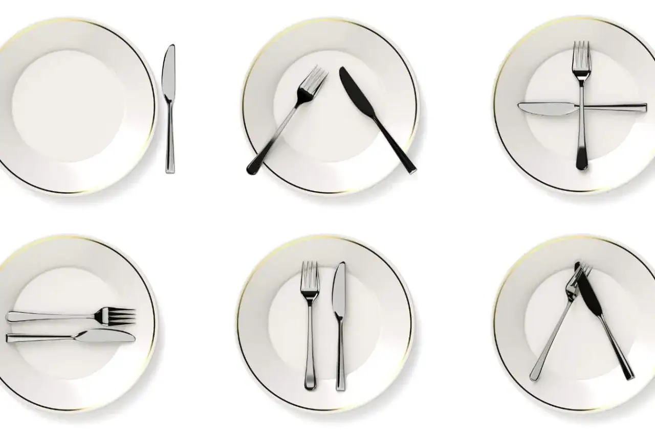 Six assiettes blanches avec des couverts disposés différemment, illustrant la signification des couverts en fin de repas.