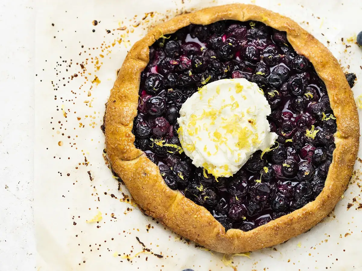 Tarte aux myrtilles traditionnelle, garnie d'une cuillère de crème et de zeste de citron. Un délice gourmand.