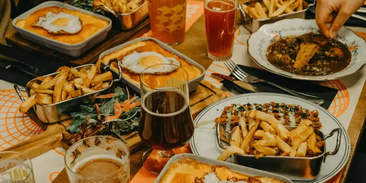 Un festin copieux dans une ambiance de tavernes : frites croustillantes, plats gratinés, salade fraîche et bières ambrées.