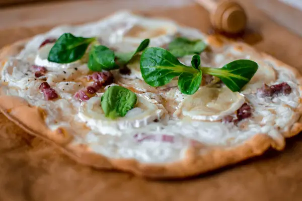 Tarte flambée alsacienne garnie de lardons, fromage de chèvre et jeunes pousses.