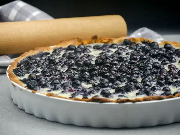 Tarte aux myrtilles traditionnelle, garnie de fruits frais et d'une crème onctueuse, prête à être dégustée.