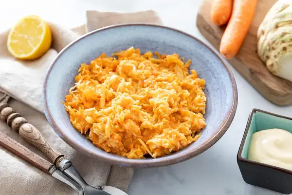 Un bol de carottes râpées originales, avec un quartier de citron et une coupelle de mayonnaise à côté.