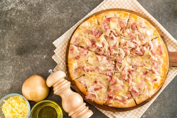 Flammekueche gourmande, garnie de lardons et d'oignons sur une base de fromage blanc crémeux. Un délice croustillant.